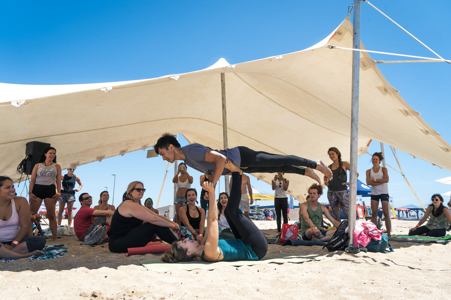 A yoga class under a cream stretch tent on the beach