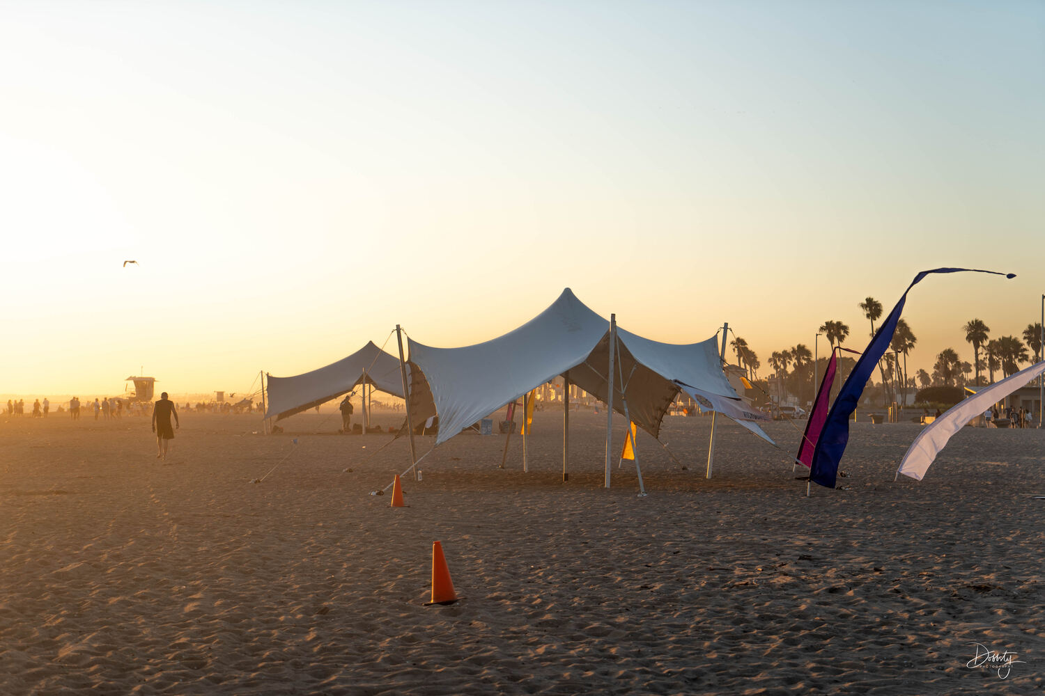 A group seated under a cream stretch tent on the sand
