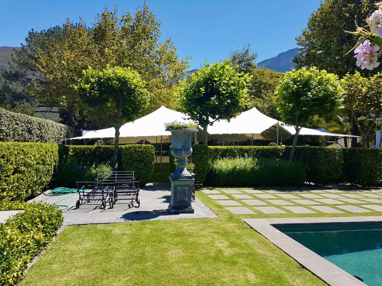 White canopies over a garden terrace beside a pool
