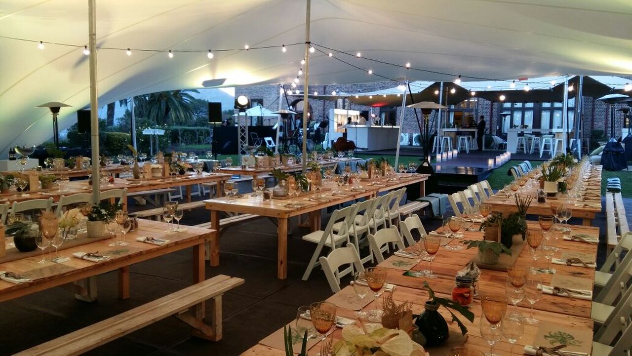 Long dining tables set under a stretch tent strung with lights