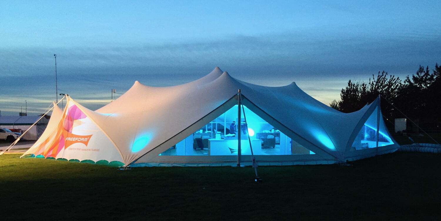 A stretch tent glowing with coloured light at dusk