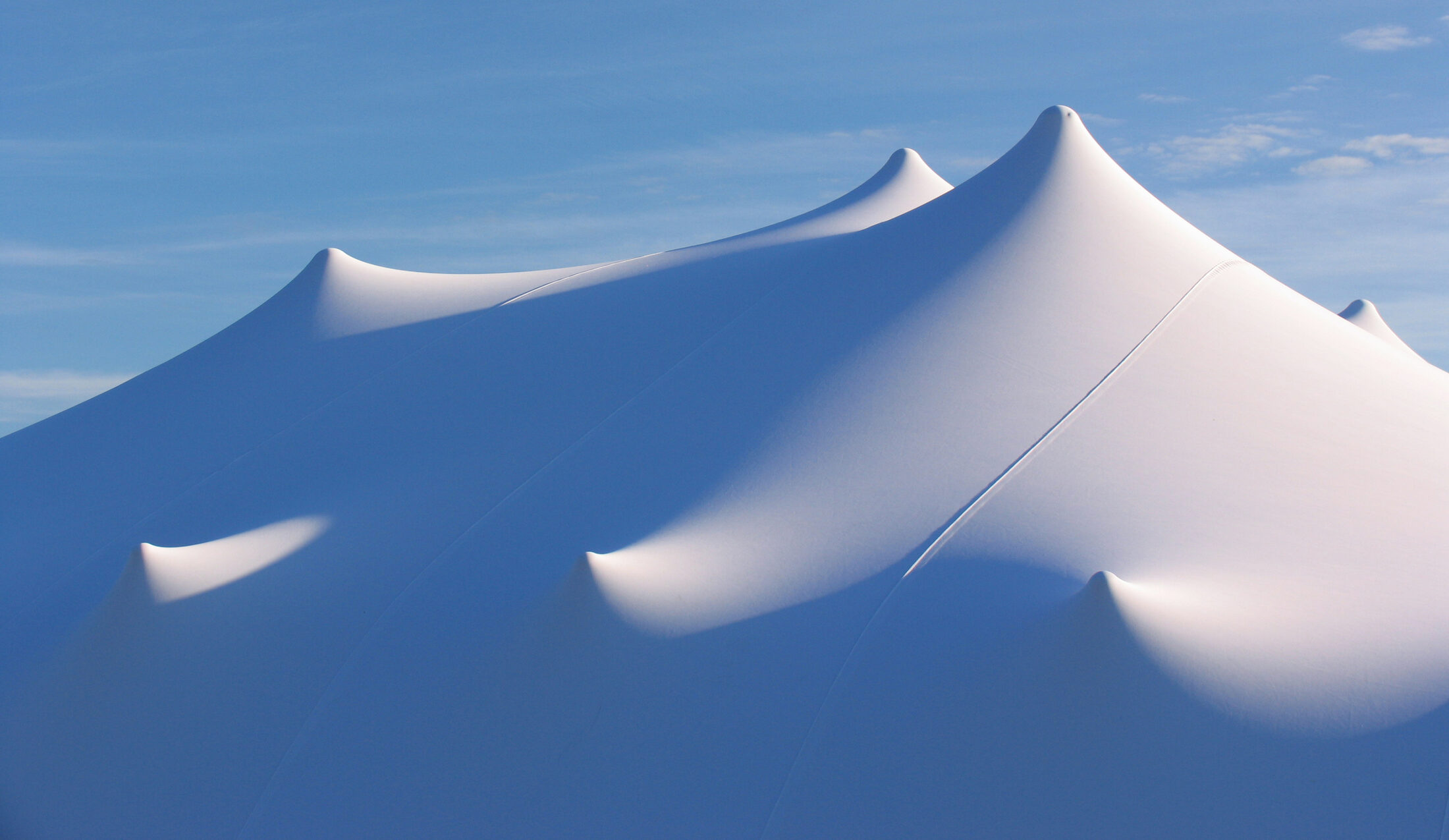 The peaks of a white Freeform stretch tent against a blue sky