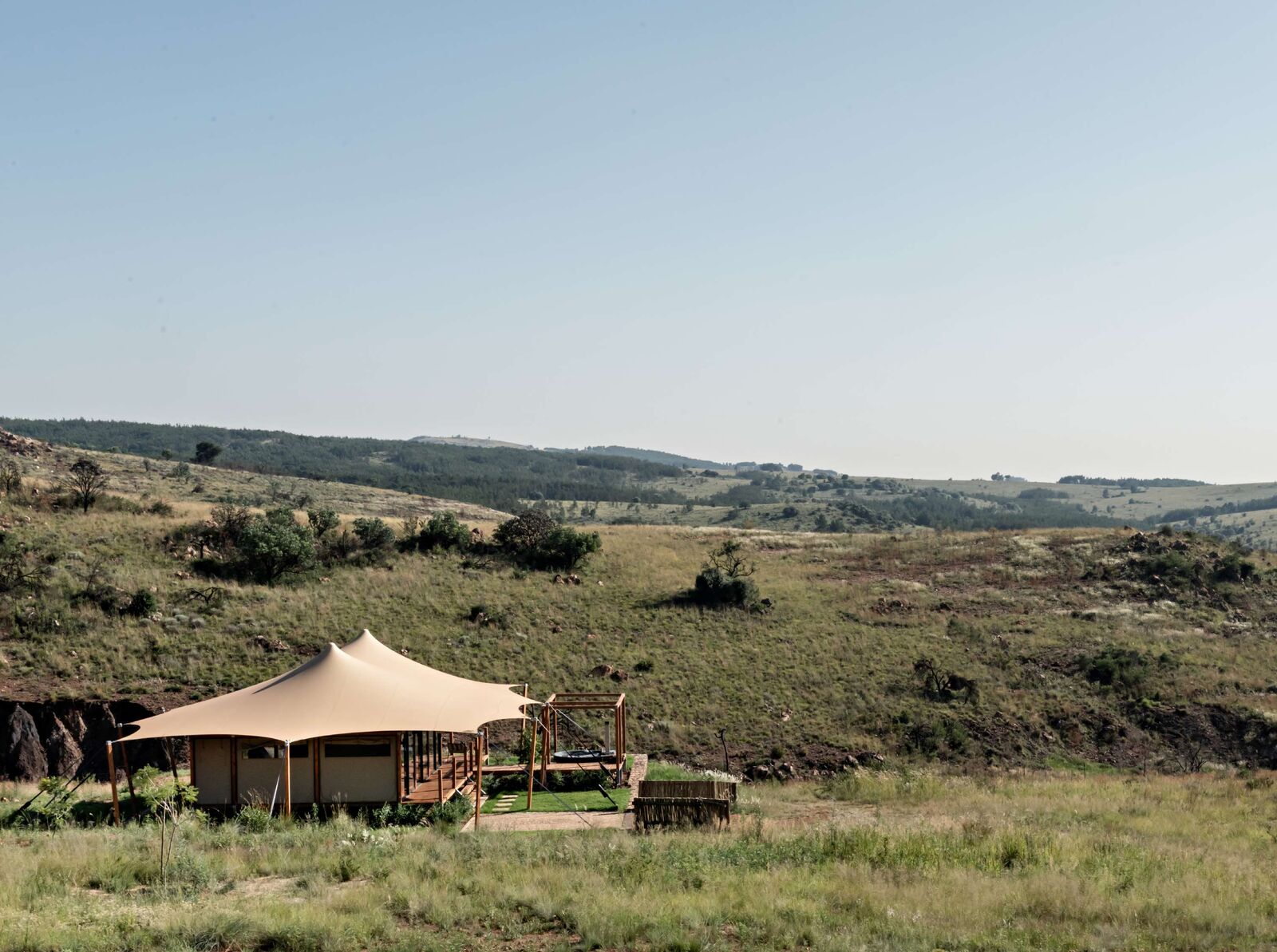 A safari tent under a chino stretch canopy in open grassland