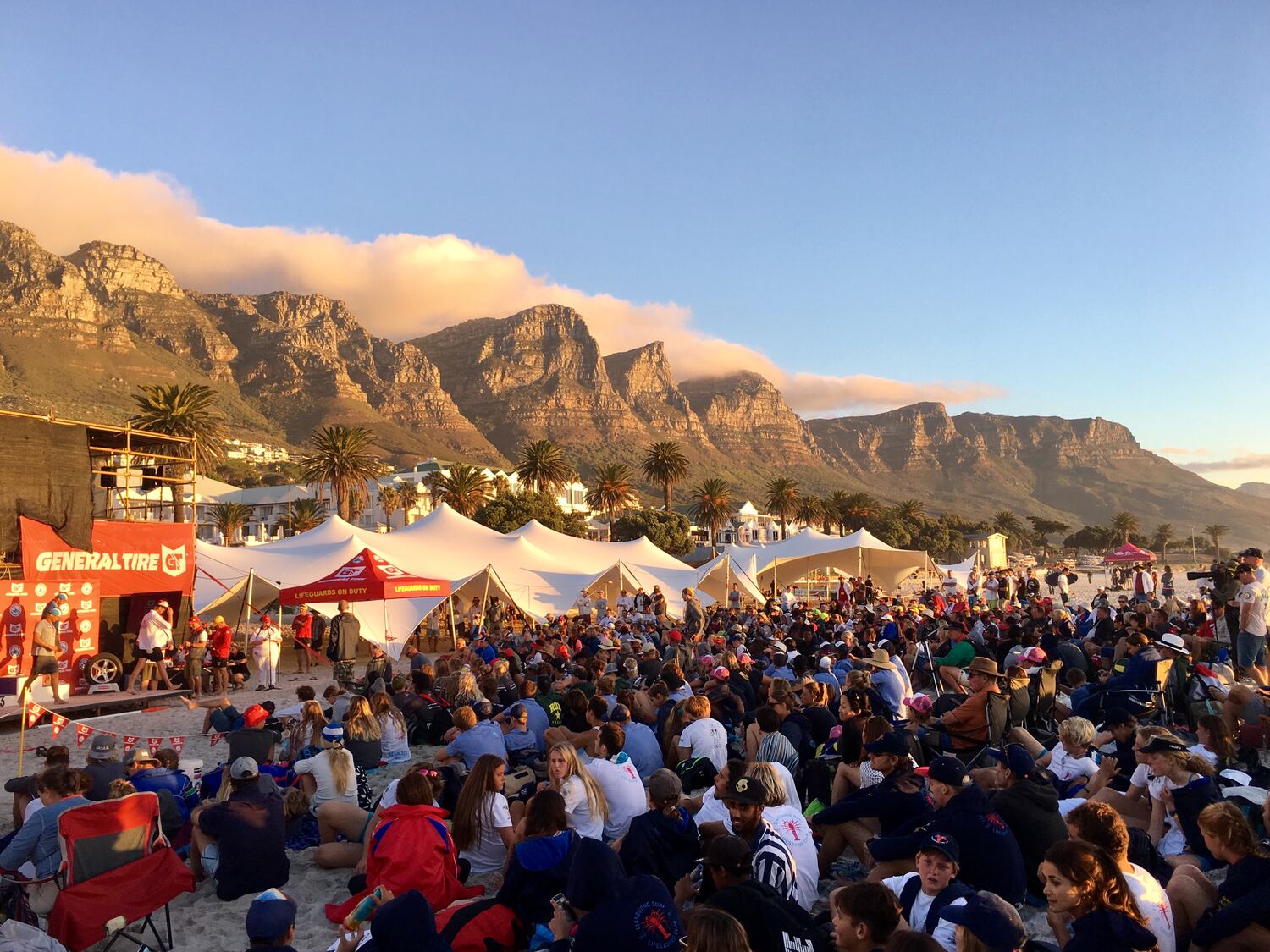 A large crowd seated under linked stretch tents