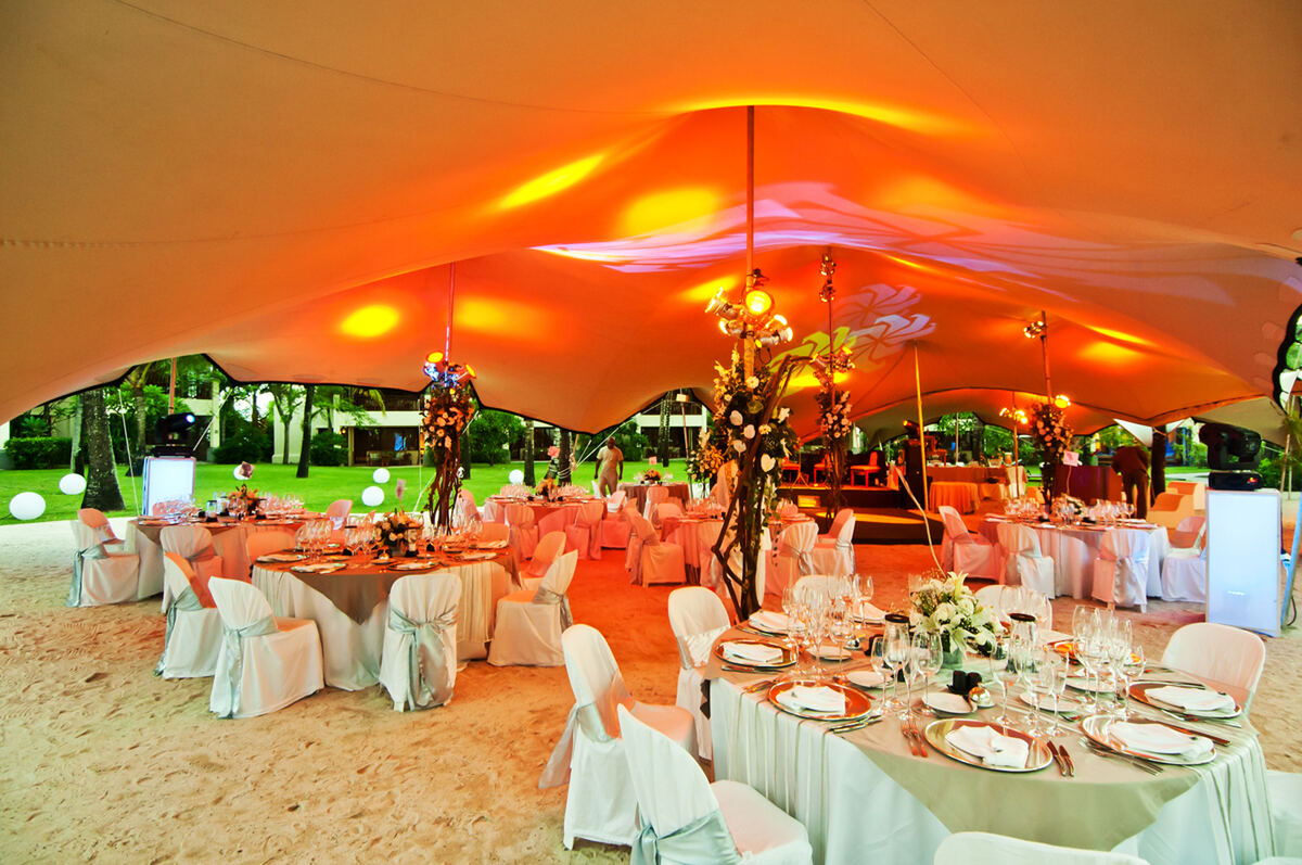 A wedding dinner under a warmly lit stretch tent